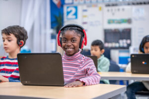 A female elementary student on her laptop with headphones in class