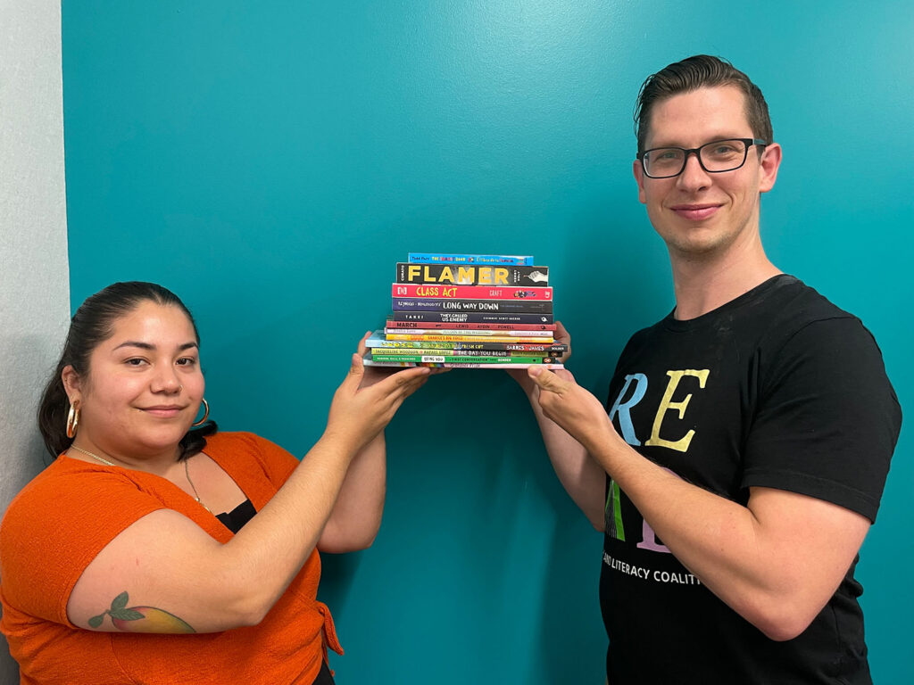 Two staff members at Oakland Literacy Coalition hold a stack of children's books that have been banned in the United States