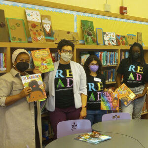 Four staff members from the Oakland Literacy Coalition hold up their favorite children's books in a library in Oakland